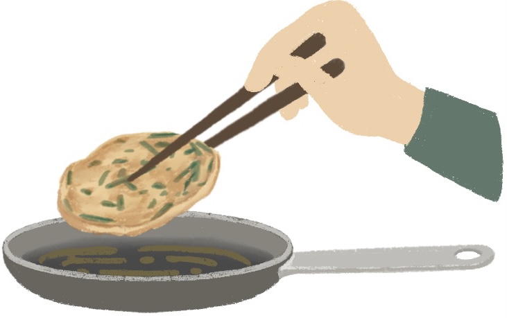 hands holding chopsticks and flipping a Korean pancake in a pan